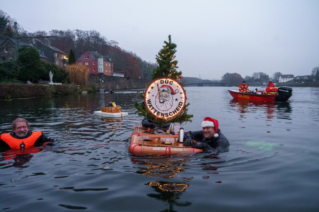 Ein Schwimmer mit Weihnachtsm&uuml;tze, der  sich an einem Flo&szlig; mit Weihnachtsbaum festh&auml;lt